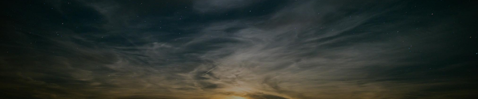 Calm ocean at sunset revealing wispy clouds and dark starry sky.