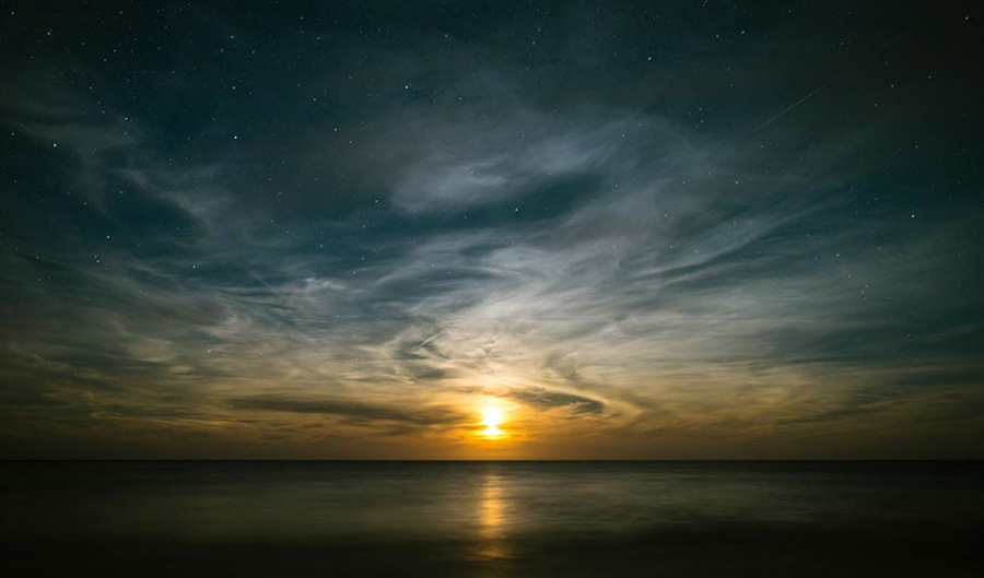 Calm ocean at sunset revealing wispy clouds and dark starry sky.