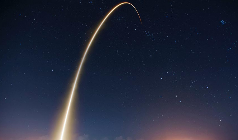 Rocket flies into the dark starry sky leaving a yellow glow behind as it leaves Earth's atmosphere. 